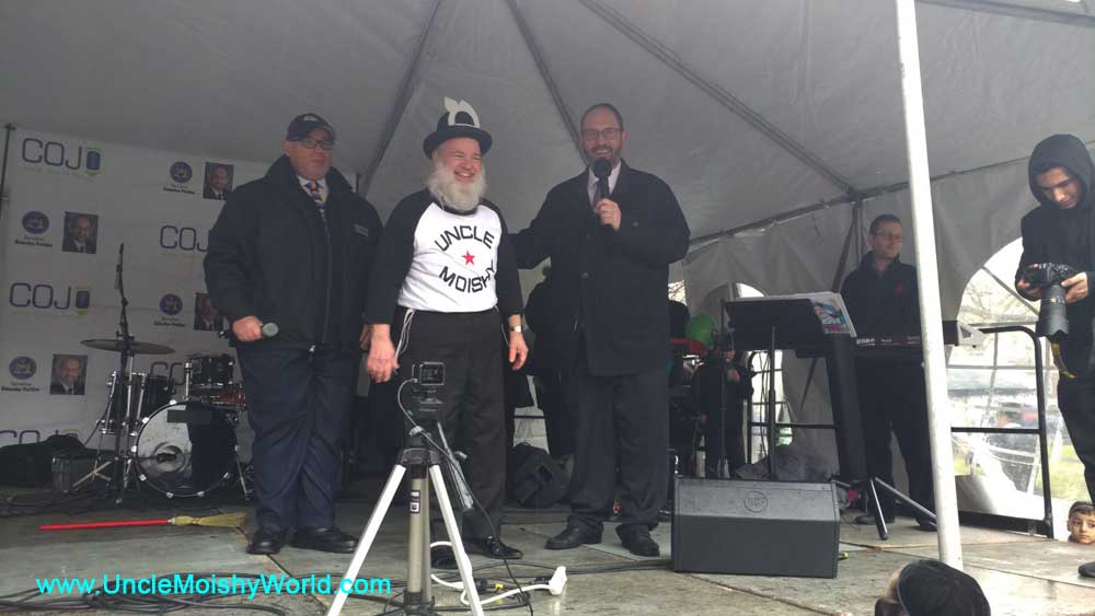 Moishy Tanenbaum on stage with friends posing for a photo.