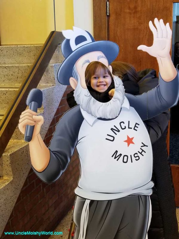 A darling child over layed on a life-size stand up of Uncle Moishy.